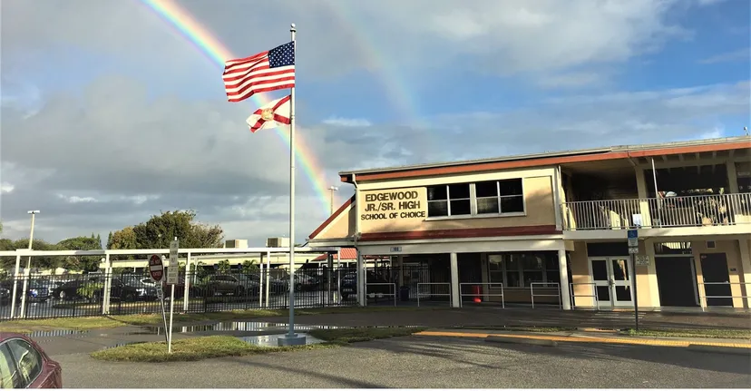 Davanti all'edificio scolastico delle Brevard County Public Schools, la bandiera americana e quella dello Stato sventolano sotto un arcobaleno nel cielo nuvoloso.