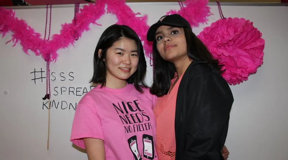 Due studentesse della Summerland Secondary School posano davanti a una parete con grandi decorazioni di piume rosa.