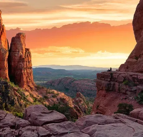 Persona seduta su una sporgenza rocciosa guarda un canyon di roccia rossa al tramonto