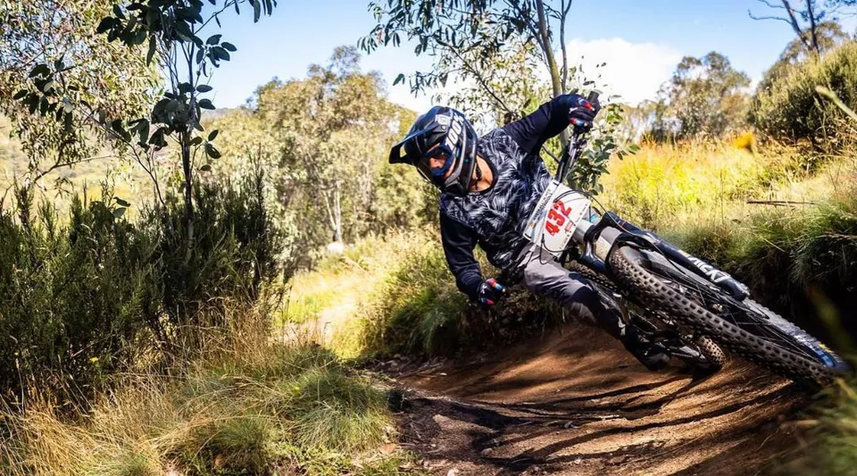 Una persona in abbigliamento mimetico guida una dirt bike su un sentiero boschivo tortuoso all'interno del terreno della Cronulla High School.