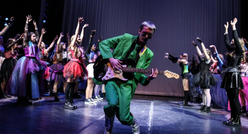 Un musicista in abiti verdi suona sul palco davanti a un gruppo di danza nel campus del Castlepollard Community College.