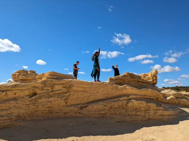 Tres jóvenes de pie sobre una gran roca de arenisca bajo un cielo azul despejado