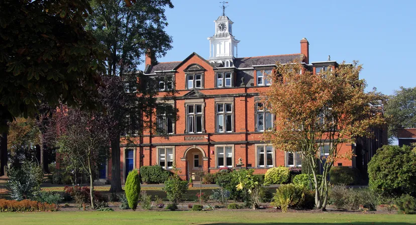L'edificio storico in mattoni con l'alta torre dell'orologio si trova nel campus di Wrekin College circondato da un verde paesaggio.