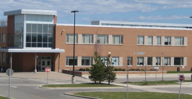 Das moderne Gebäude der Donald A. Wilson School mit Backstein- und Glasfassade steht vor einem klaren blauen Himmel.