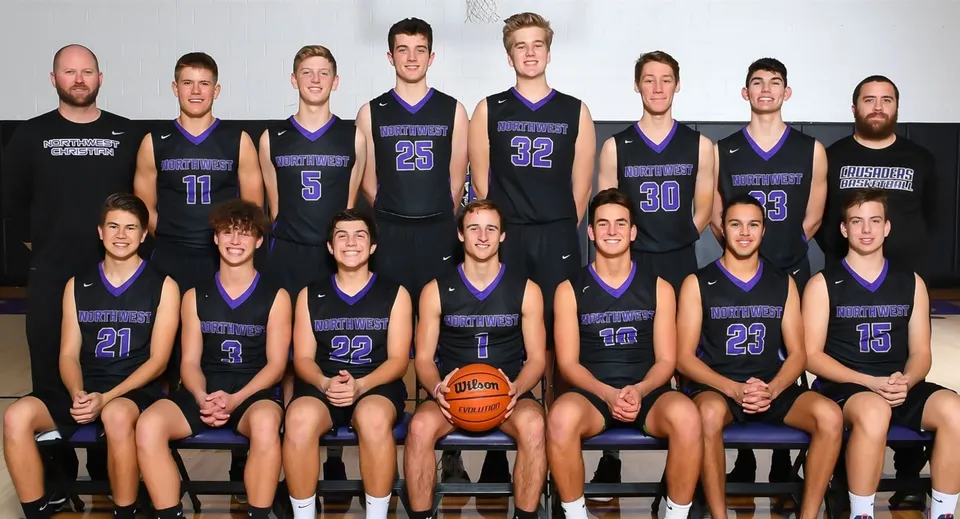 La squadra di pallacanestro della Northwest Christian High School posa insieme nella palestra indossando maglie viola e nere.