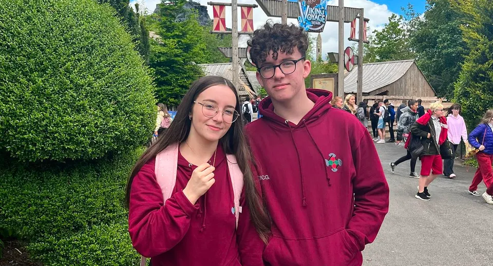 Due persone stanno in piedi su una strada con diversi edifici sullo sfondo nell'area della St. Ciarán’s Community School.