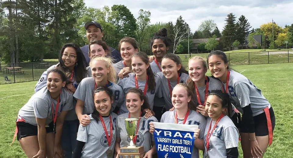 Un gruppo di giovani atlete della Markham District High School festeggia con un trofeo su un campo da gioco.