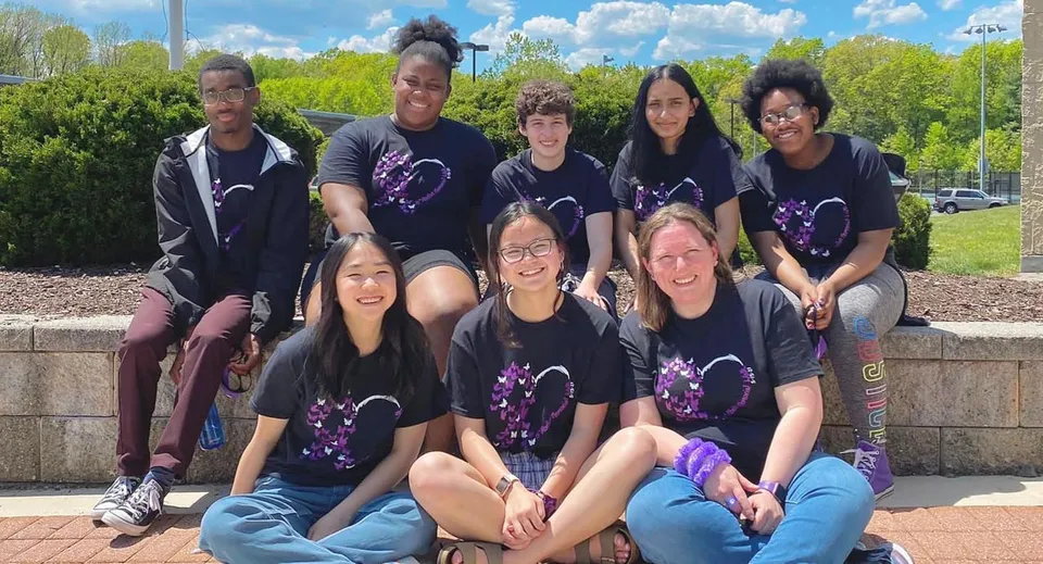Un gruppo di studenti e studentesse della Connecticut IB Academy in posa insieme all'aperto davanti a degli alberi.