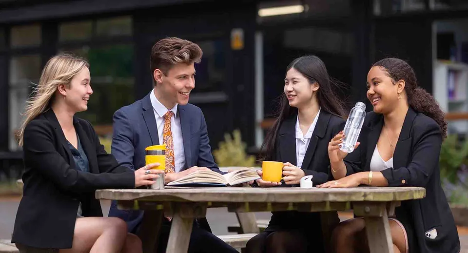 Quattro giovani conversano attorno a un tavolo all'aperto nel campus del Stoke College.