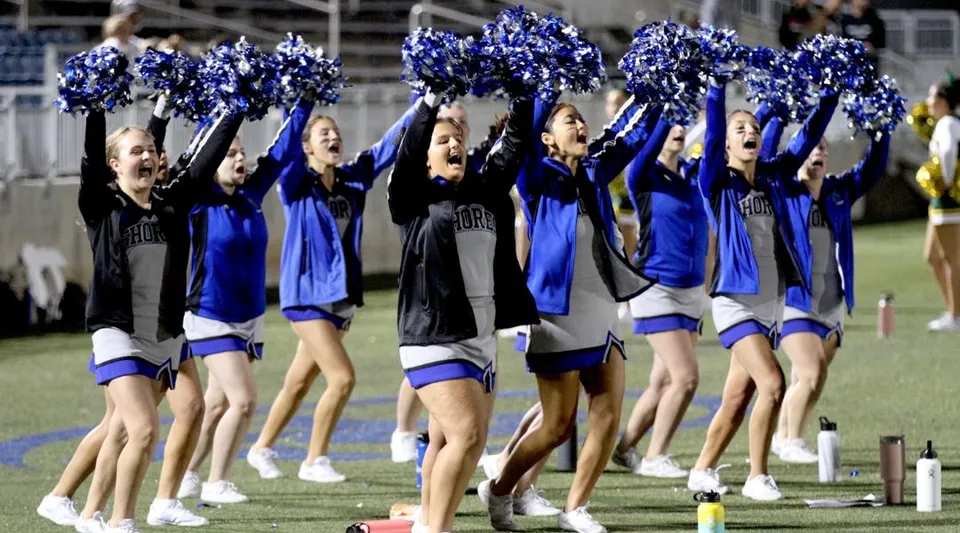 Un gruppo di cheerleader della Atlantic Shores Christian School esegue una coreografia sul campo sportivo davanti agli spettatori.