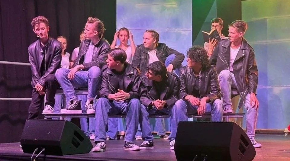 Un gruppo di studenti siede sul palco della Stepaside Educate Together Secondary School davanti a uno sfondo colorato.
