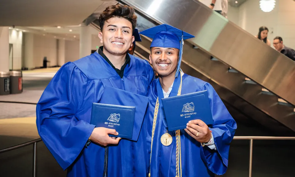 Due studenti del Denver Public School District sono nel corridoio in toga blu da diploma e mostrano con orgoglio i loro diplomi.