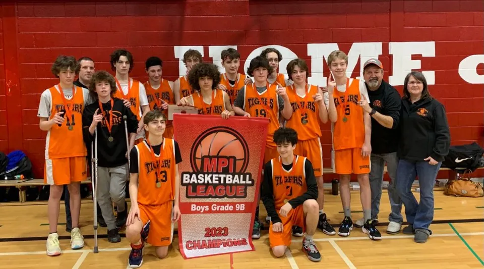 Un gruppo di giovani giocatrici e giocatori di basket della Holy Trinity High School tiene insieme un trofeo di campionato in palestra.