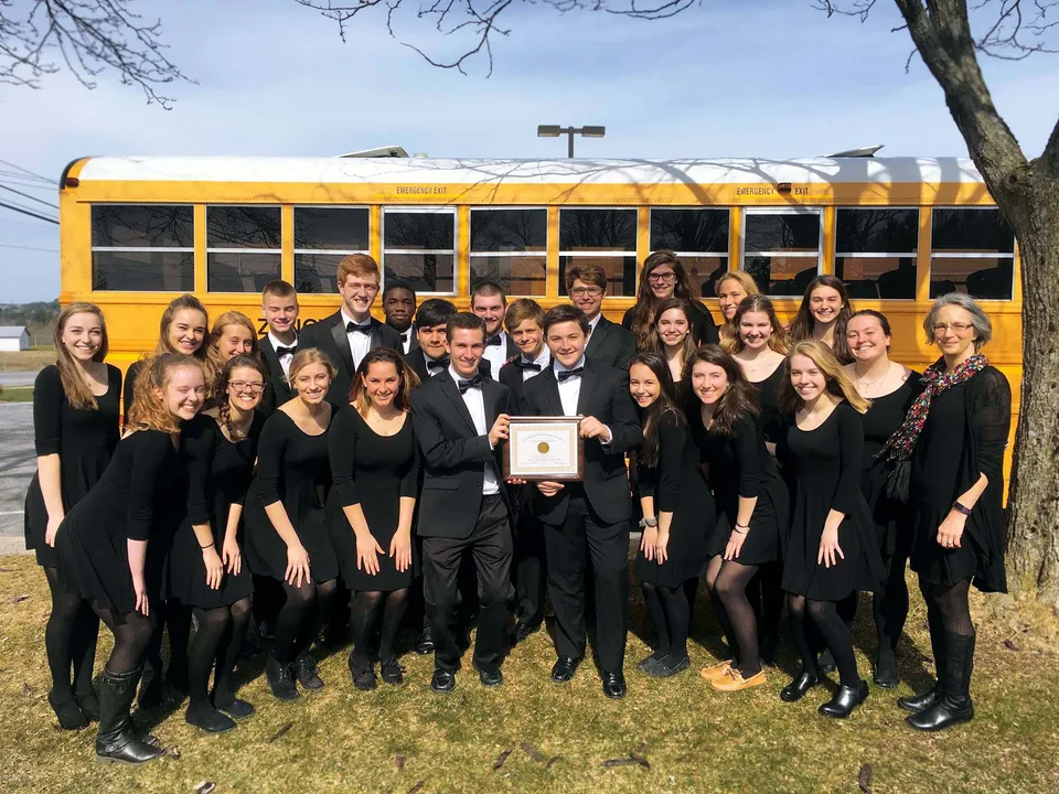 Un gruppo di studenti della Fabius Pompey High School posa davanti a uno scuolabus giallo.