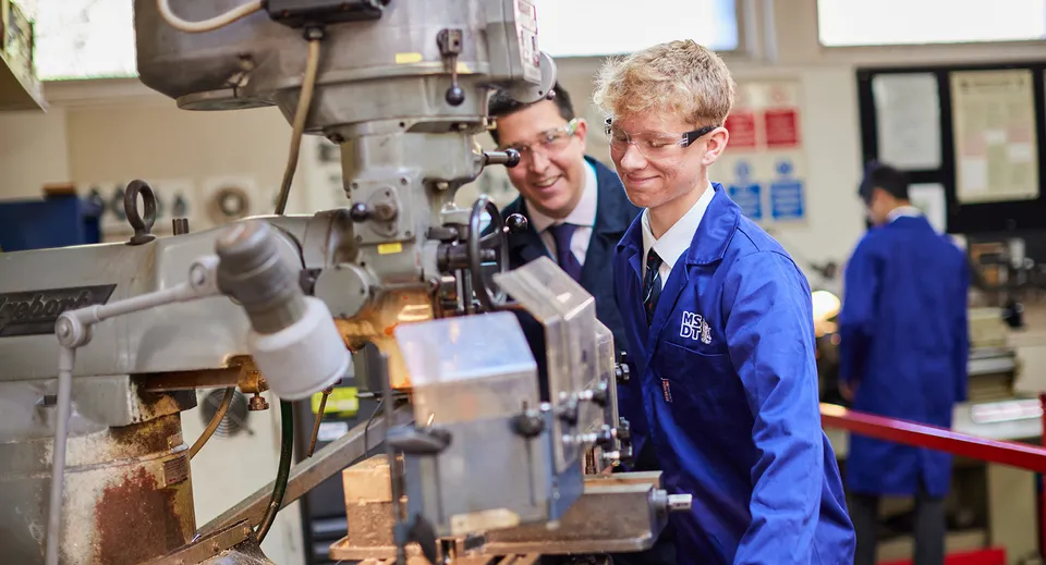 Due studenti delle Haberdashers' Monmouth Schools lavorano insieme a un grande macchinario industriale in officina.