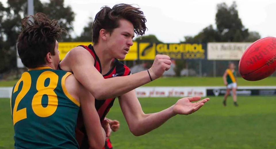 Uno studente della Murray Bridge High School corre con un pallone da football su un campo sportivo con un tabellone segnapunti sullo sfondo.