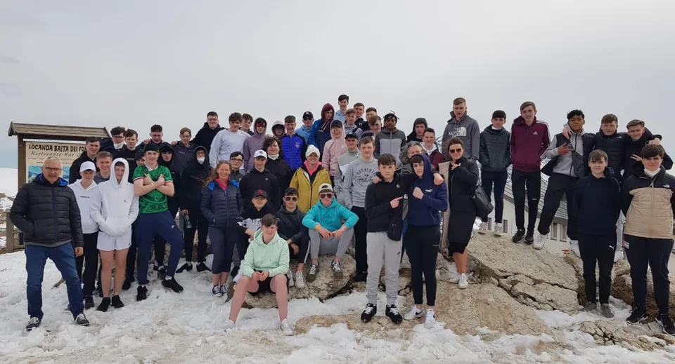Un grande gruppo di persone si trova insieme in un paesaggio innevato sotto un cielo nuvoloso al Garbally College.