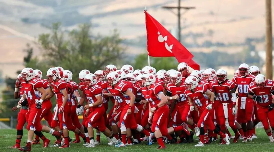 Un gruppo di giocatori di football in divisa rossa con una bandiera rossa sul campo sportivo dell'Ashland School District.