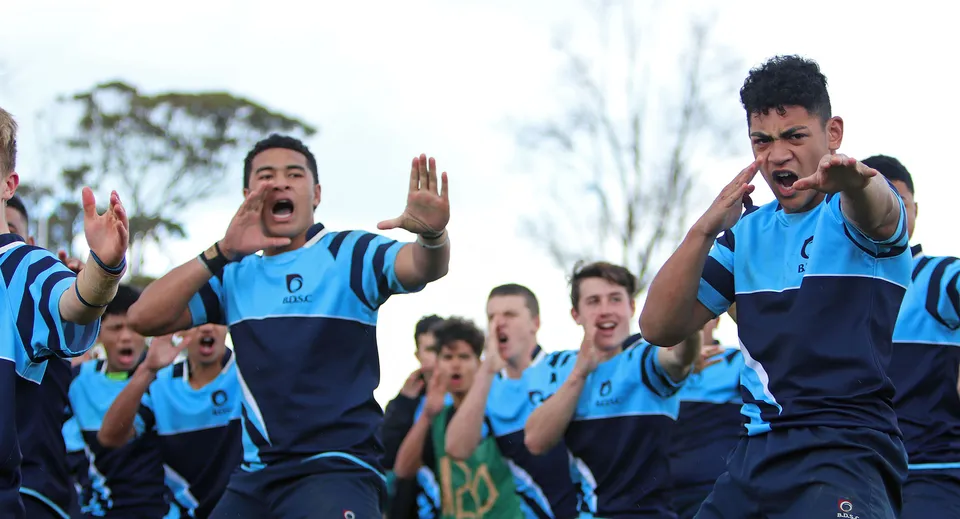 Un gruppo di studenti del Botany Downs Secondary College festeggia sul campo sportivo con le proprie divise sportive blu.