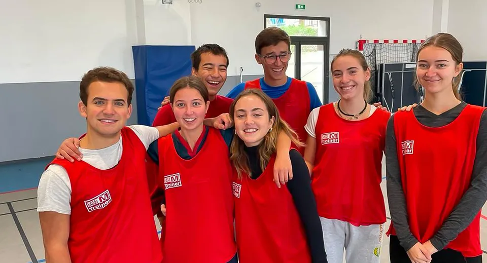 Un gruppo di studenti e studentesse della International Bilingual School of Provence in maglia rossa posa nella palestra.