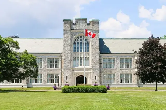 Storico edificio scolastico in pietra con bandiera canadese sulla torre e prato verde in Canada
