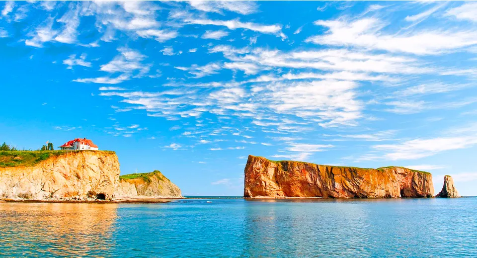 Scogliere rocciose rossastre e una grande formazione rocciosa nel mare blu sotto un cielo sereno.