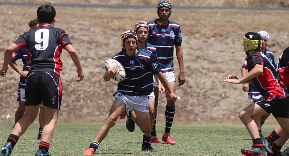 Studenti della Mountain Creek State High School giocano una partita di rugby su un campo d'erba verde sotto un cielo blu.