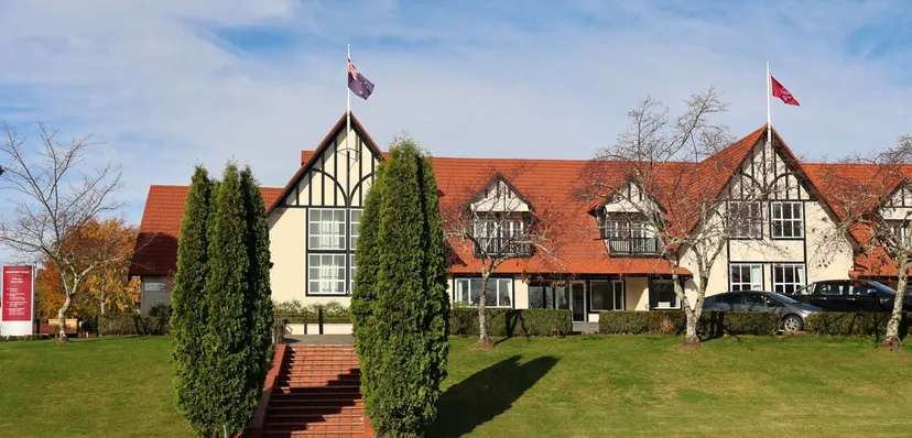 L'edificio in stile Tudor di Woodford House si trova su un prato curato, circondato da cipressi e due bandiere nazionali.