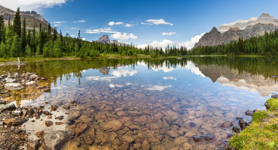 Un tranquillo lago di montagna circondato da foreste sempreverdi e vette innevate sotto un cielo azzurro.