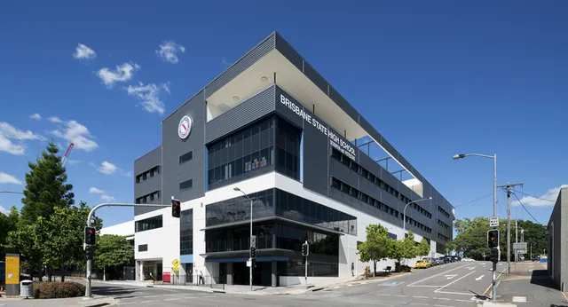Das moderne Gebäude der Brisbane State High School steht vor Bäumen unter klarem blauen Himmel.