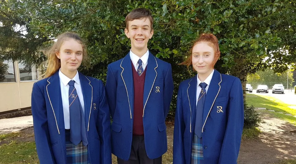 Tre studenti in divisa scolastica si trovano all'aperto davanti a un prato verde nel campus della Rookwood School.