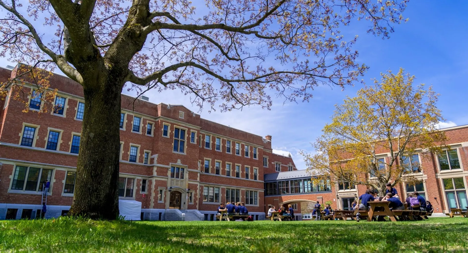 Studenti seduti a tavoli da picnic davanti agli edifici in mattoni del campus della Bishop’s College School.