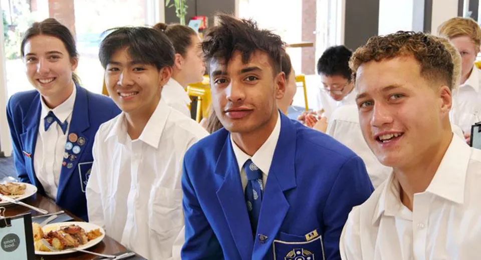 Gli studenti del Saint Kentigern College sono seduti insieme a un tavolo e mangiano nella mensa della scuola.