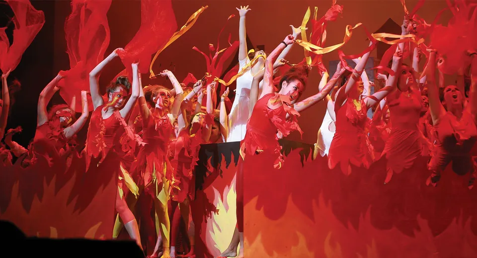 Un gruppo di ballerine e ballerini dell'Avondale College mette in scena una performance dinamica con costumi rossi e gialli.
