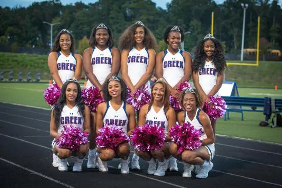 Un grupo de cheerleaders posa con uniformes morados y blancos en el campo deportivo de Mallard Creek High School.