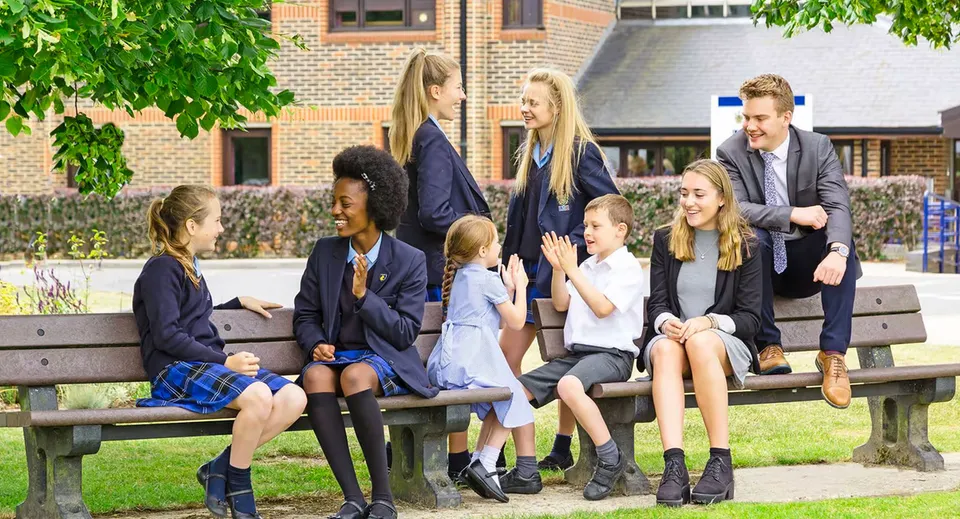 Un gruppo di studenti e studentesse siede su una panchina davanti a un edificio in mattoni nel campus della LVS Ascot.