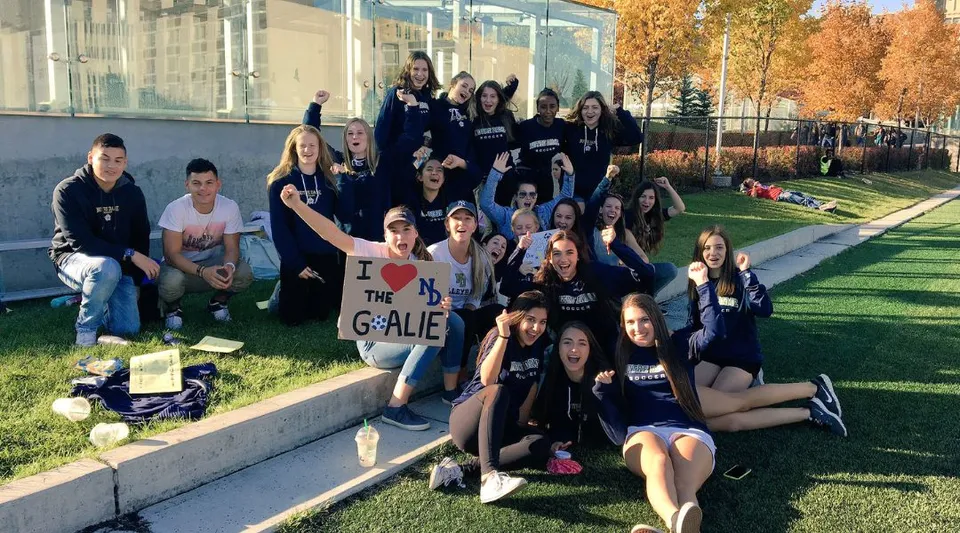 Un gruppo di studenti della Notre Dame High School a Calgary è seduto e in piedi su un prato davanti a un edificio scolastico.