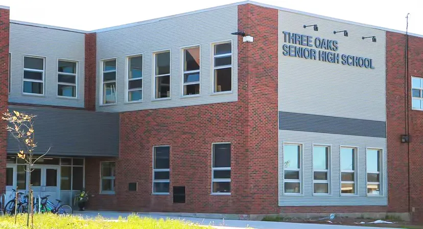 L'edificio moderno della Three Oaks Senior High School, con facciata in mattoni e vetro, è circondato da una vegetazione curata.