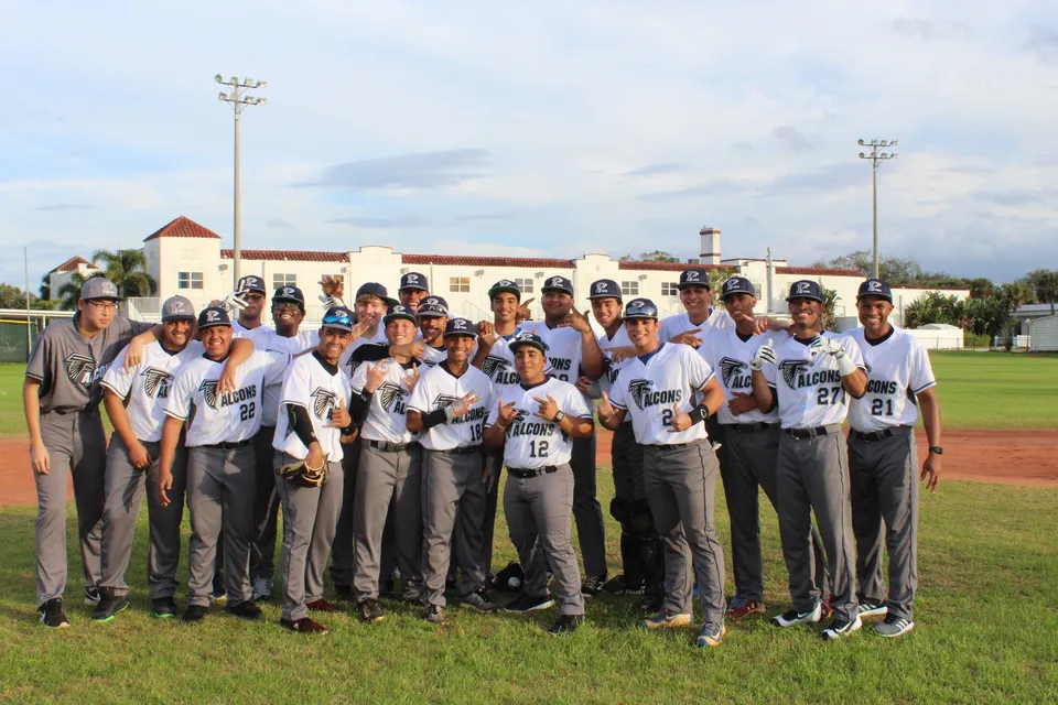 Un gruppo di giocatori e giocatrici di baseball della Florida Preparatory Academy sul campo da baseball davanti a un edificio con illuminazione sportiva.