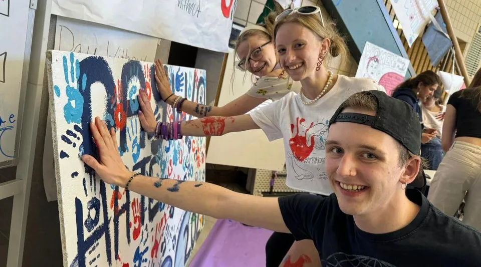 Tre giovani della Jeffco Public Schools mettono le mani sporche di pittura su una tela dipinta insieme.