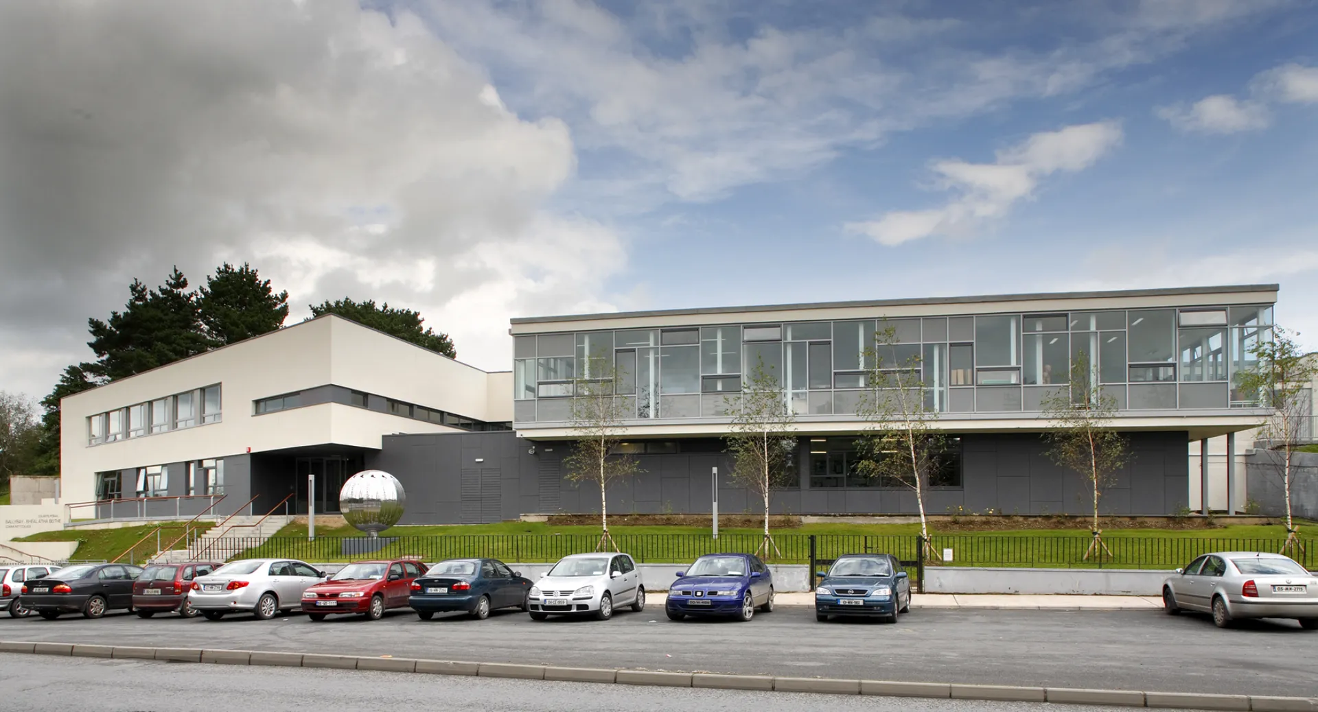 L'edificio moderno del Ballybay Community College con facciata in vetro e un parcheggio in primo piano.