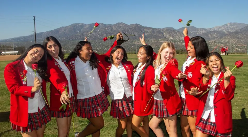 Studentesse della Flintridge Sacred Heart Academy festeggiano in toga da diploma rossa e bianca davanti a un paesaggio montano.