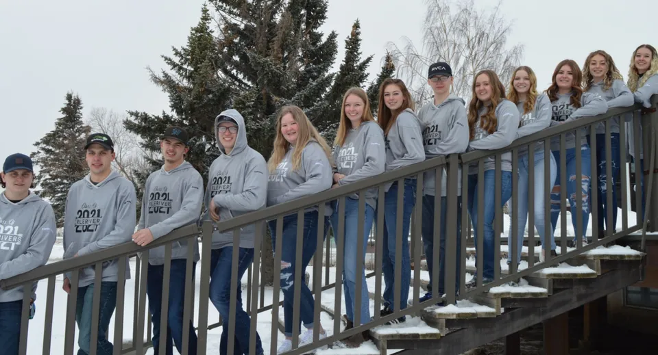 Studenti della J.T. Foster High School si trovano su un balcone di legno con alberi innevati sullo sfondo.