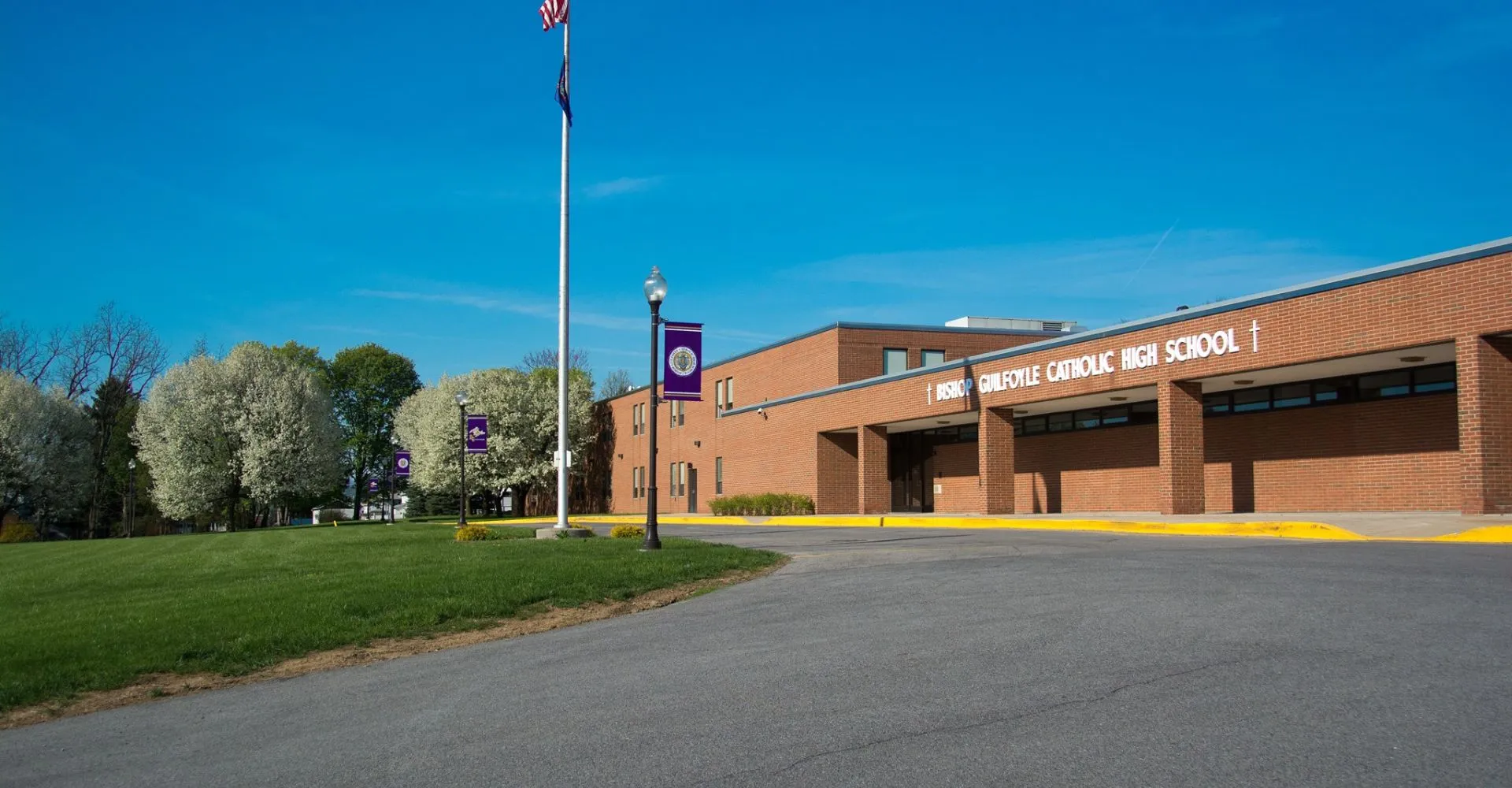 L'edificio in mattoni della Bishop Guilfoyle Catholic High School con un'asta per bandiera davanti a un prato e alberi sotto un cielo azzurro.