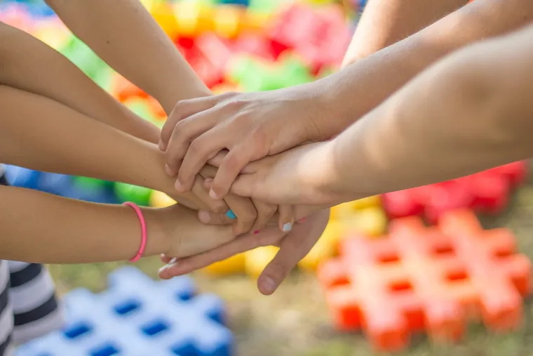 Kinderhände liegen übereinander, im Hintergrund bunte Bausteine