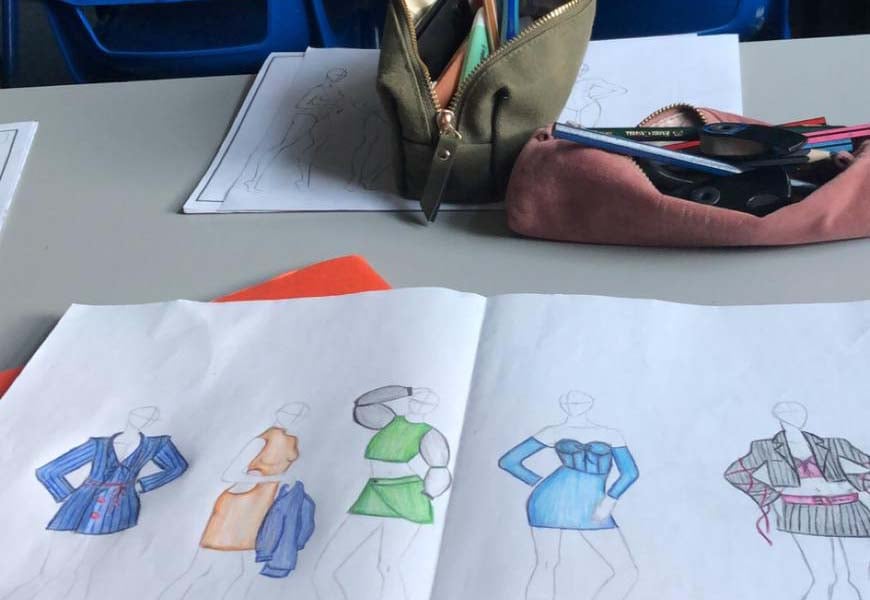 Selbst gezeichnete Modeentwürfe und Federmäppchen auf einem Schultisch