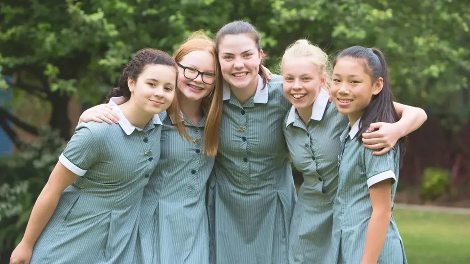 Un gruppo di studentesse del Methodist Ladies' College in divisa scolastica verde si trova insieme in un'area verde all'aperto.