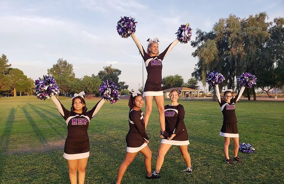 Studenti della Mission Heights Preparatory High School durante un'esibizione di cheerleading su un campo erboso con alberi sullo sfondo.