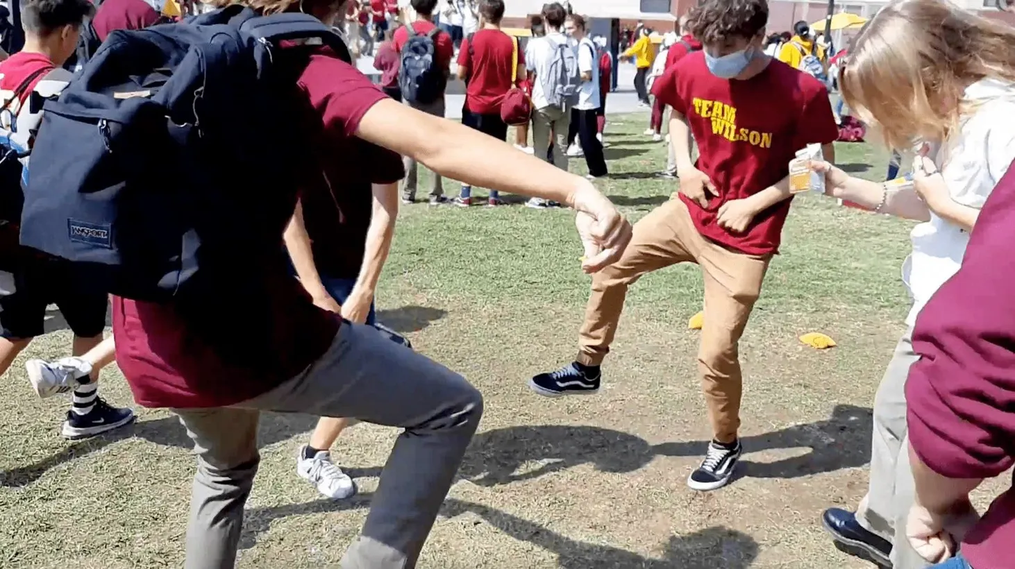 Grupo de estudiantes de instituto con camisetas granates jugando en el césped del patio del colegio al sol