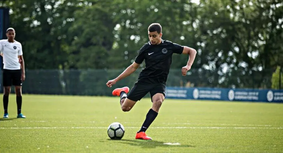Un calciatore in maglia nera corre con il pallone sul campo del St. Bricin’s College.